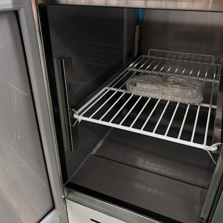 Interior view of a KRD Saladette Prep Table 3 doors Granite Pizza top 8x GN 1/6 Depth 700mm 400L showing wire shelving.