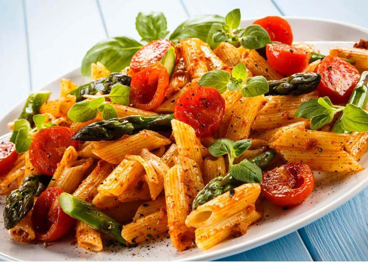 Penne pasta dish with cherry tomatoes and asparagus on a white platter, garnished with basil.